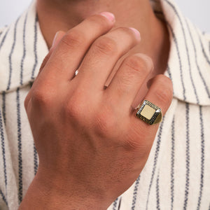 The 14K Gold Square Black Enamel Greek Key Signet Ring For Men features a square face embellished with a detailed black enamel Greek key pattern, echoing the labyrinthine meander design. Its bold, symmetrical style emphasizes the textured center, providing a stunning contrast between the black and gold elements.