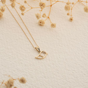 The 14K Solid Gold Bird Necklace, featuring a diamond eye, glistens on its delicate chain against a white background, showcasing the elegance of fine gold jewelry.