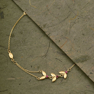 Introducing the 14K Solid Gold Ruby Butterfly Bracelet from the Chloris Collection, featuring a delicate chain design with small red beads and leaf-shaped charms. This exquisite bracelet is embellished with butterfly accents, making it an ideal choice for those celebrating a July birthstone.