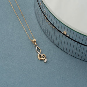 The 14K Solid Gold Treble Clef Necklace by RundaJewelryUs features a striking pendant that artfully combines gold and silver tones, making it an elegant piece of music-themed jewelry that stands out beautifully against a white background.