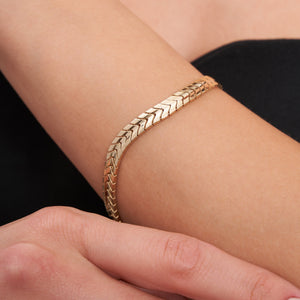 The 14K solid gold snake bracelet, with a smooth, glossy finish and secure clasp, forms an elegant circle. Its intricate pattern reflects light beautifully, showcasing the allure of exquisite gold jewelry.