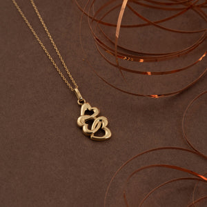 The 14K Solid Gold Trio Heart Pendant Necklace by RundaJewelryUs is crafted in 14K yellow gold and features a pendant with three interlocking heart shapes. The elegant design is suspended from a delicate chain, highlighting the shiny gold finish with a commitment to sustainable methods.