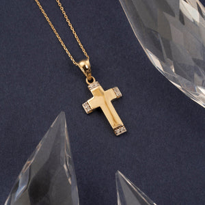 This minimalist jewelry piece is the 14K Gold Tiny Cross Necklace by RundaJewelryUs, featuring a chain with diamond-like stones embellishing the top and bottom edges of the cross. It's a timeless religious accessory elegantly showcased against a plain white background.