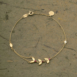 Introducing the 14K Solid Gold Ruby Butterfly Bracelet from the Chloris Collection, featuring a delicate chain design with small red beads and leaf-shaped charms. This exquisite bracelet is embellished with butterfly accents, making it an ideal choice for those celebrating a July birthstone.