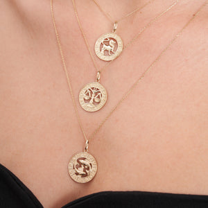 The 14K Gold Astrology Zodiac Charm Necklace by Runda Jewelry features a solid gold chain and a circular pendant adorned with an astrology zodiac symbol. The intricate detailing along the edge adds elegance to this charming necklace, set against a plain white background.